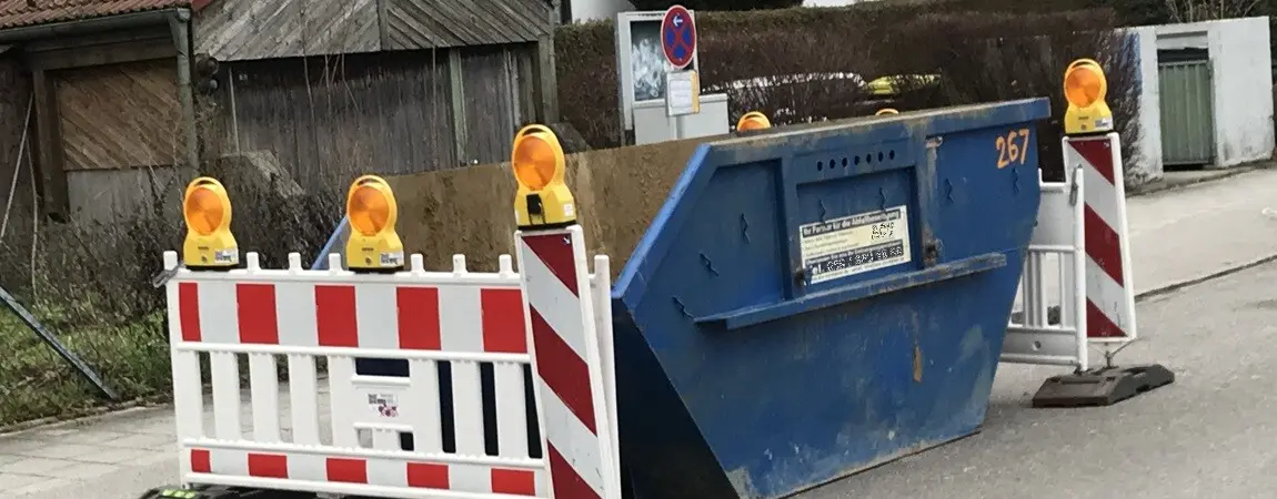 Absicherung eines Schuttcontainers in München mit Baken und Absperrzäunen.